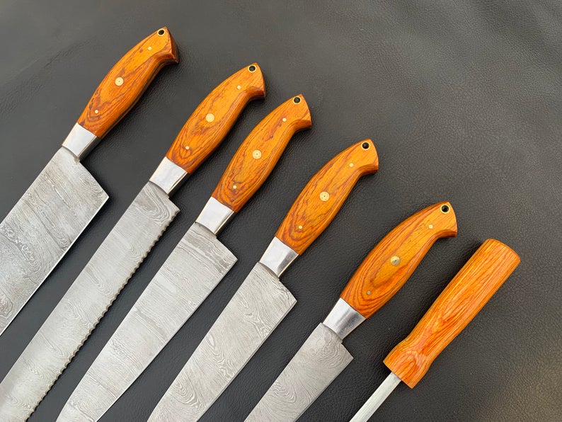 Damascus steel knife set with sharpening rod fanned on black background