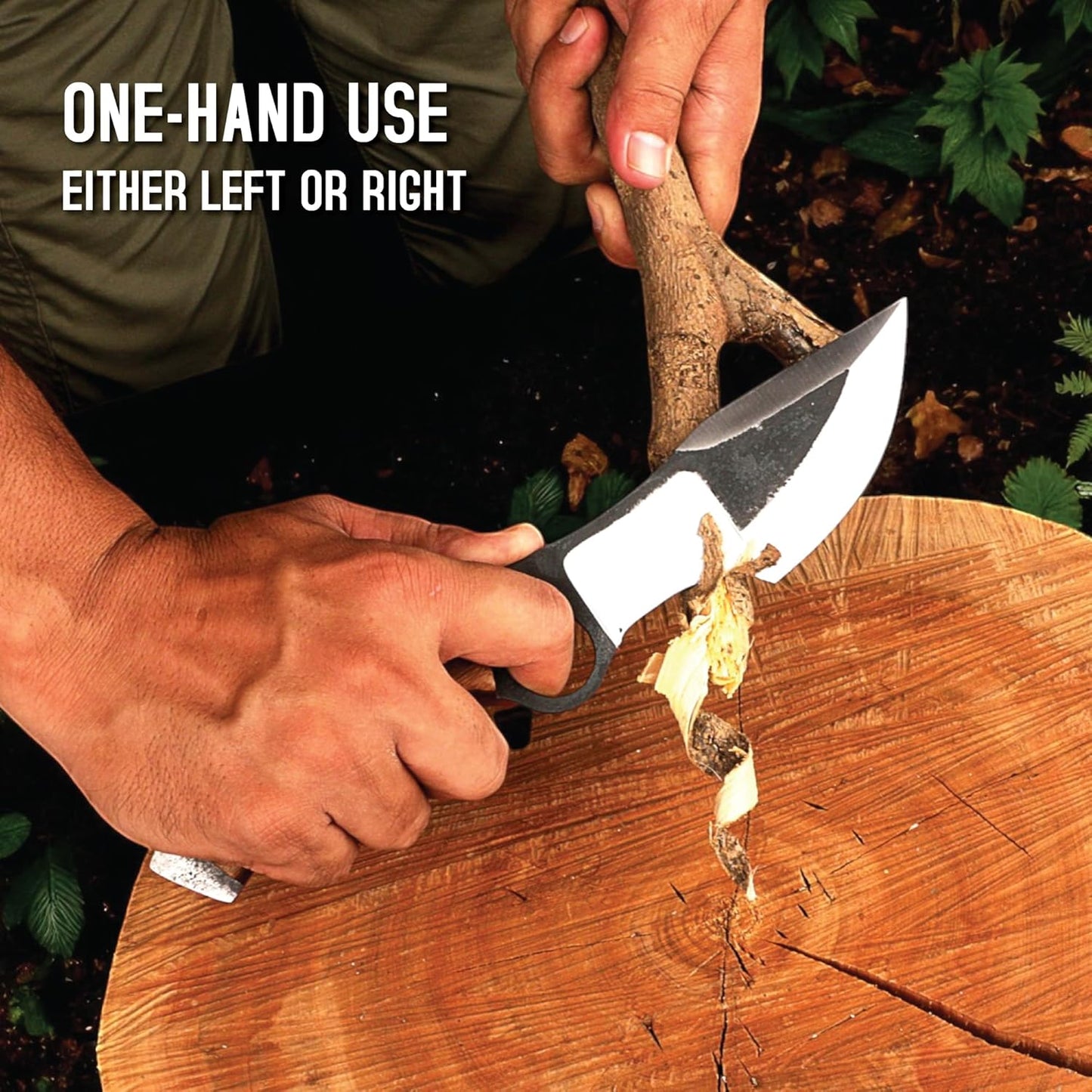 An action shot showing a person's hands carving a thick branch over a large, heavily textured wooden stump using a hunting tracker knife. The person's left hand grips the wooden handle, with their index finger secured securely through the large circular hole in the dark metal section of the blade for control. The highly polished silver cutting edge is actively shaving a thick, curling strip of wood from the branch held in their right hand. In the upper left corner, white text reads 'ONE-HAND USE' and 'EITHE