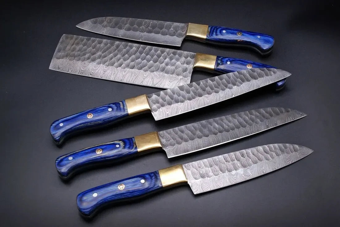 Five Damascus kitchen knives with blue handles laid out on a dark background