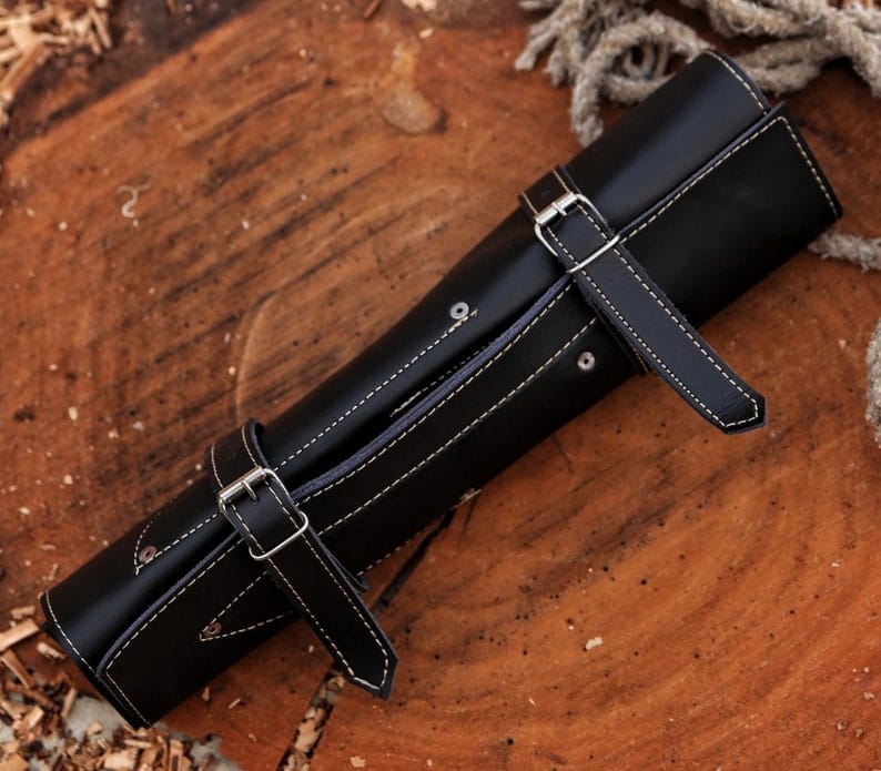 Black leather knife roll case with buckle straps on wood stump