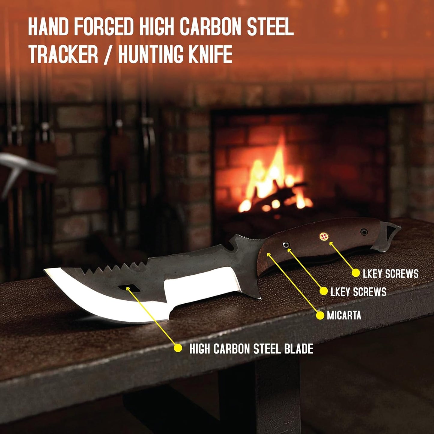 A survival tracker knife resting horizontally on a dark, textured surface, such as an anvil or metal bench, against a warmly lit, softly blurred background featuring a brick fireplace with a burning fire. The knife showcases a dark brown handle with an exposed lanyard pommel and a distinctive two-toned blade: a matte black upper section with a serrated spine and a teardrop cutout, paired with a polished silver cutting edge. Bold white text in the upper left corner reads 'HAND FORGED HIGH CARBON STEEL TRACKE